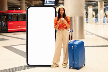 In a bustling airport, a young woman stands beside a large blank advertisement display while...