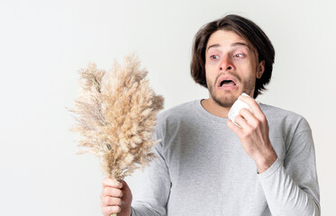 Shocked man holds grass and sneezes in napkin in hand
