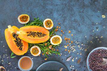Slices of sweet papaya, passion fruit and rucola surrounded by granola flakes on a stone background