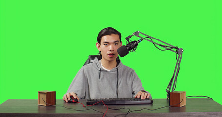 Young streamer broadcasting gameplay while he is sitting at workstation playing online action games with people. Young video blogger gaming live for stream at pc with microphone.