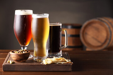 Glasses with different types of beer and snacks on wooden table in bar. Space for text