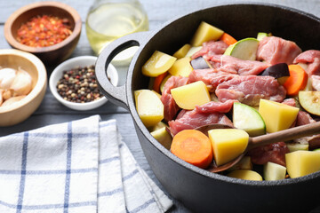 Cooking stew. Uncooked meat and vegetables in pot on light grey wooden table, closeup
