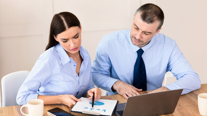 Business Partnership. Two Coworkers Working Together Using Laptop And Charts Sitting At Desk In Modern Office.