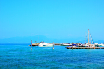 Pristine view at the Port of Peschiera del Garda with white yachts, white and blue motorboats neatly docked and ready to skim the slightly rippling azure waters with blue shades under a spotless sky