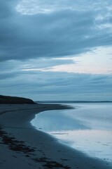 Serene coastal landscape at dusk with calm waters and cloudy sky.