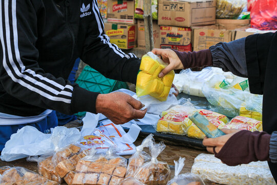 Cimahi, Indonesia - August 21, 2024: A bustling Indonesian street market scene. A vendor and customer interact, exchanging money for food products. The vibrant energy of daily life is captured.
