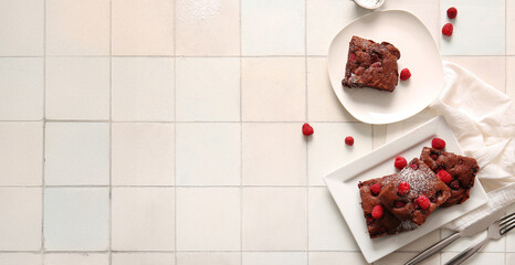Plates with pieces of raspberry chocolate brownie on white tile background