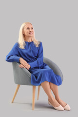 Mature woman sitting in armchair on grey background