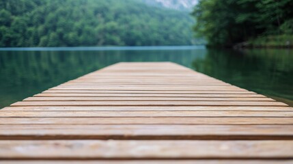 Fototapeta premium A serene wooden dock extends into a calm lake surrounded by lush greenery and mountains, inviting tranquility and reflection.