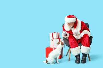 Santa Claus with cute Jack Russell Terrier dog and Christmas gift boxes on blue background