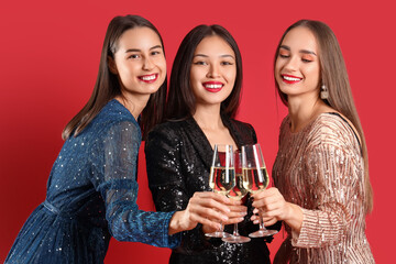 Beautiful young women with champagne on red background. New Year celebration