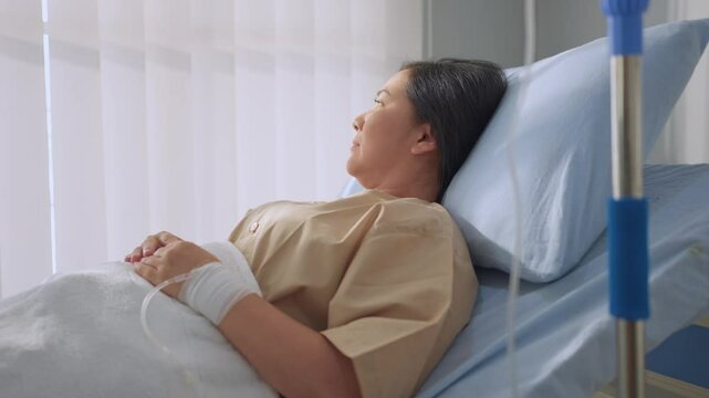 Asian mature female patient getting saline solution in hospital ward. 
