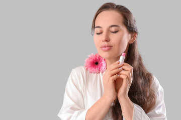Young woman with lip balm and gerbera flower on grey background, closeup