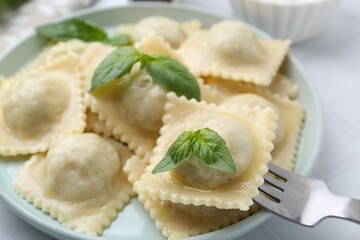 Taking delicious ravioli with cheese and basil from plate at table, closeup