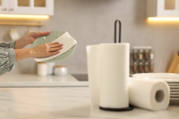 Woman wiping plate with paper towel at white marble table in kitchen, closeup