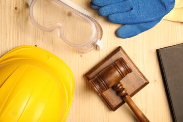 Accident at work concept. Gavel, book and protective gear on wooden table, flat lay