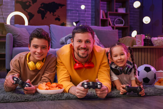 Happy father with his little children playing video game on floor at home in evening