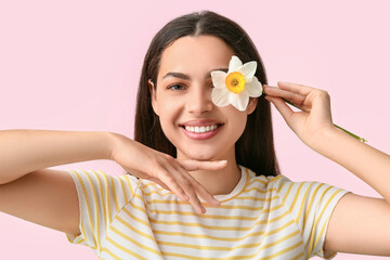 Beautiful young woman with daffodil flower on pink background