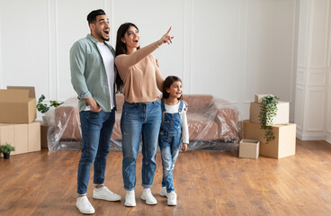 Cheerful amazed Middle Eastern family of three people enjoying moving in new apartment, excited...