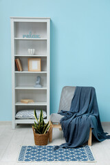 Armchair with plaid, plant and shelving unit near blue wall
