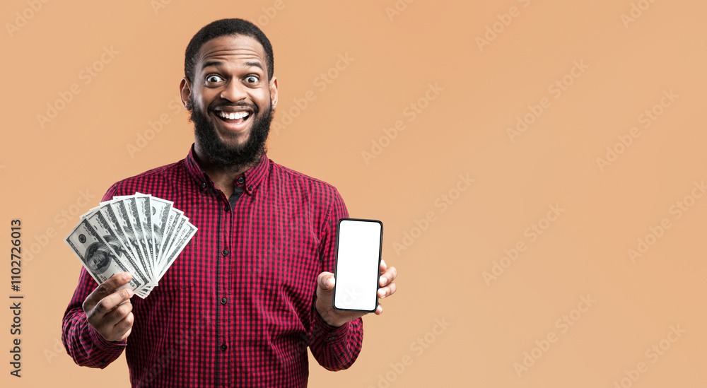 Poster Black surprised man holding mobile phone with blank empty screen and fan of cash money in dollar banknotes in hand posing isolated on yellow background. People and finance concept. Mock up copy space.