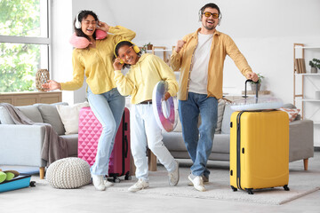 Happy family in headphones with packed suitcases for travel at home