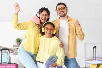 Happy family in headphones with packed suitcases and inflatable ring for travel at home