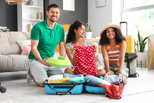 Happy family sitting on floor and packing suitcase for travel at home - Powered by Adobe
