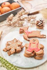 Festive Christmas cookies displayed on a white plate, including gingerbread shapes of a reindeer, a snowflake, and a gingerbread man with icing decorations. The scene is surrounded by holiday decor, s