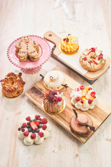 A stunning display of artisan holiday desserts arranged on wooden boards and a pink cake stand, featuring intricate and creative designs. The assortment includes a gingerbread macaron on a plate