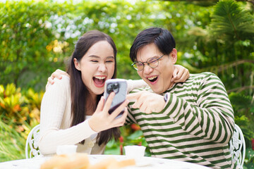 Excited Asian man and woman expressing their happy and satisfied emotion after got a message on smartphone.