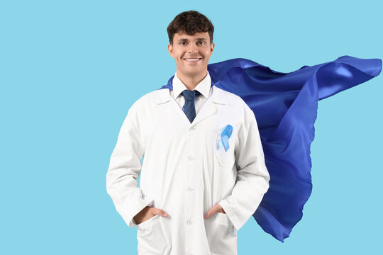 Male doctor in superhero cape with blue ribbon on color background. Prostate cancer awareness concept