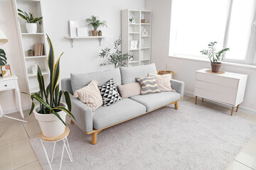 Interior of light living room with grey sofa, commode and shelf units