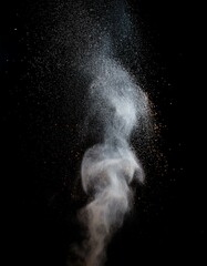 Abstract powder explosion against a black background. Whitish grey particles in motion.