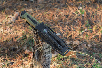 Tactical knife with a green handle in the forest. Tool against the natural leather.