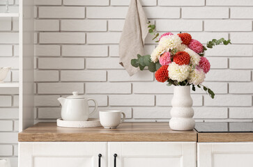 Vase with beautiful dahlia flowers and tea set on wooden kitchen counter near light brick wall