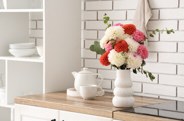 Vase with beautiful dahlia flowers and tea set on wooden kitchen counter near electric stove