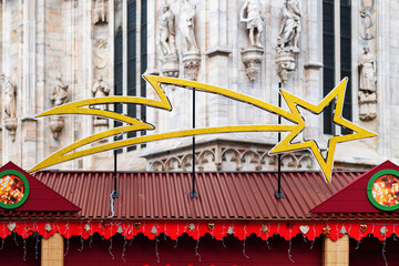 Obraz premium Large golden shooting star decoration is displayed above festive holiday market stalls. Market is set against backdrop of ornate historical building, creating charming holiday scene in city