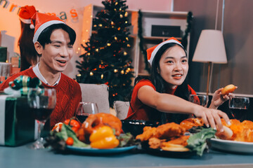 Group of young Asian man and women as friends having fun at a New Year's celebration, holding gift boxes standing by Christmas tree decoration, midnight countdown Party at home with holiday season.