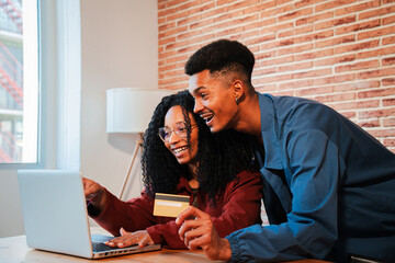 Smiling African American couple using a laptop and credit card to make an online purchase, enjoying...