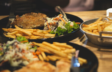 Vegetable salad and french fries and steak in a black plate on a wooden table. Select focus