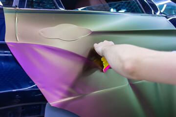 A specialist in wrapping a car with chameleon-colored vinyl film in the process of work. Car wrapping specialists cover the car with vinyl sheet or film. Car wrapping close-up. Selective focus.