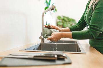 Cleaning, woman in green dress with green ceramic cup in kitchen for hygiene, routine and coffee mug. Female person, washing with water for disinfecting, protection and sink at home 