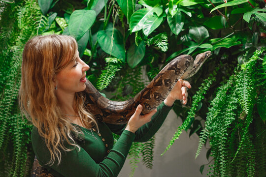 Pretty young woman holding a snake at a reptile encounter, symbolizing an exciting and educational animal interaction, against floral wall
