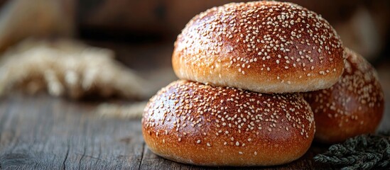 Freshly baked sesame seed bread rolls stacked on rustic wooden surface with grains in the background.