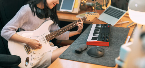 Young asian woman composer playing guitar music with digital technology at home studio