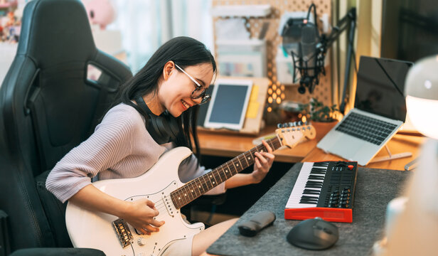 Young asian woman composer playing guitar music with digital technology at home studio - Powered by Adobe