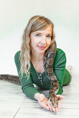 pretty  happy woman holds a snake close to her face indoor against white background
