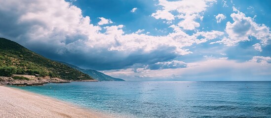 Serene beach landscape with cloudy sky and tranquil sea under soft blue hues and distant mountains in the background