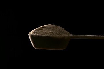 暗い背景に計量スプーンで持ち上げたプロテインパウダー